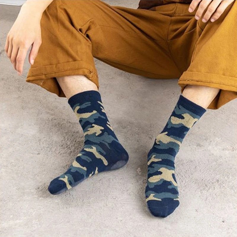 Person sitting on the floor with legs extended, wearing brown pants rolled up to mid-calf, and comfortable BlasterMaster Camo Socks.