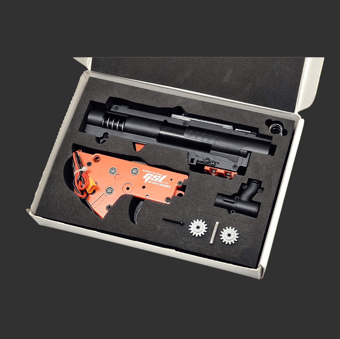 An opened box containing a disassembled Jingji GSL Metal Gearbox V2 for an airsoft SR16 & HK416D, featuring various mechanical components, including an orange gear unit, black metal parts, and two circular gears.