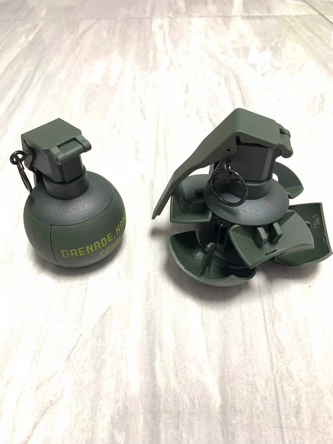 Two green hand grenade-shaped objects, one intact and the other with fins unfolded, rest on a light-colored surface. Ready to unleash chaos akin to a victory in battle, their presence hints at the explosive potential stored within the BlasterMaster G4.