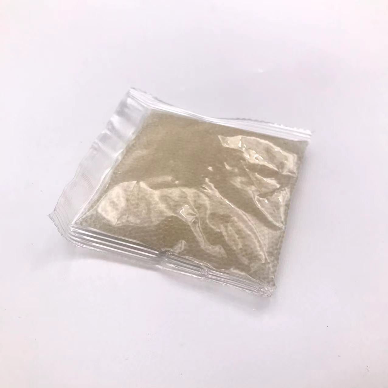 A small, clear plastic package containing a light brown, granular substance and gel balls, positioned on a white background. 

(BlasterMaster G4)