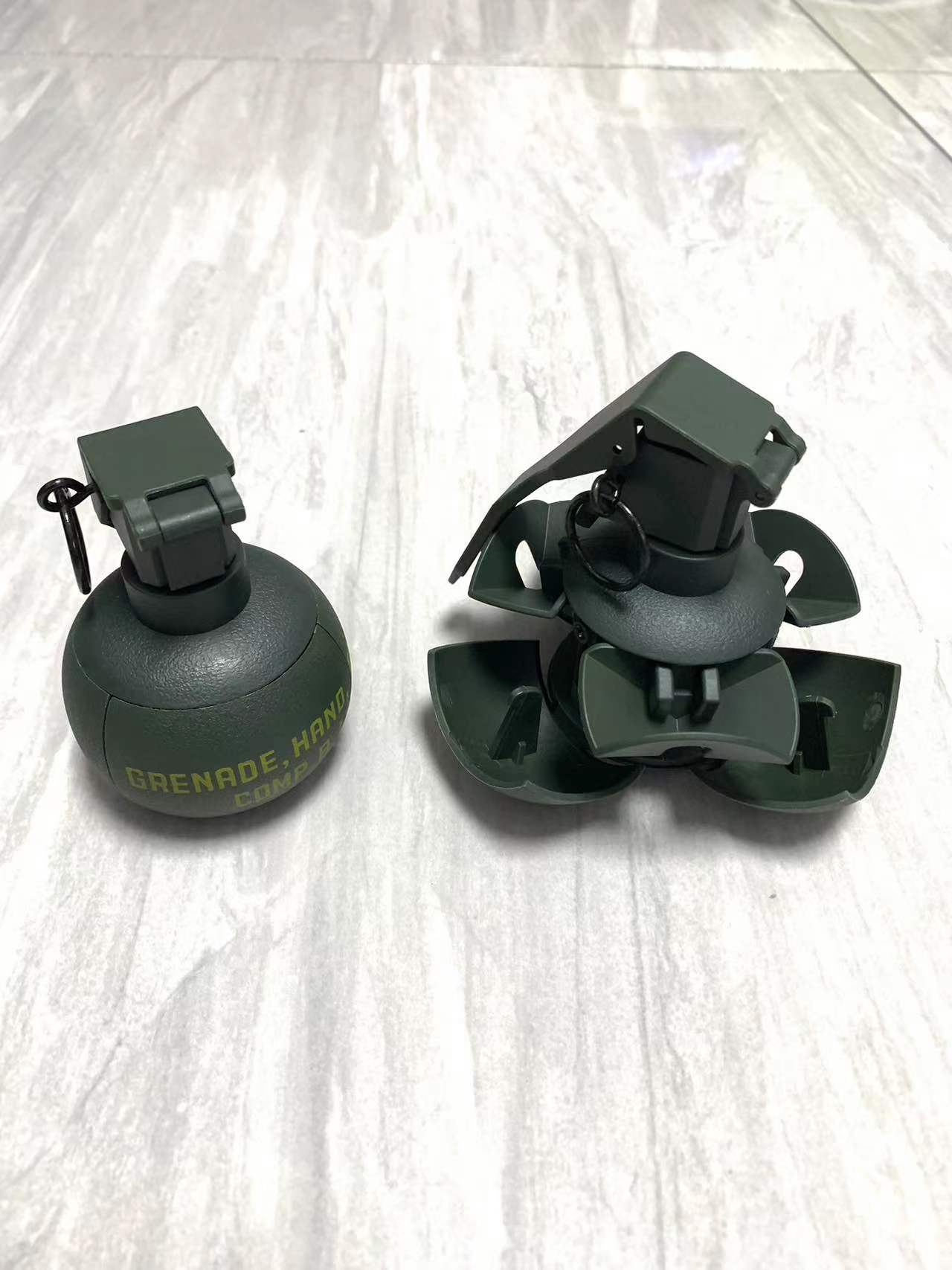 Two green BlasterMaster G4 hand grenades on a white surface. One grenade is fully closed while the other has its safety lever and clasps partially opened, ready to unleash chaos.