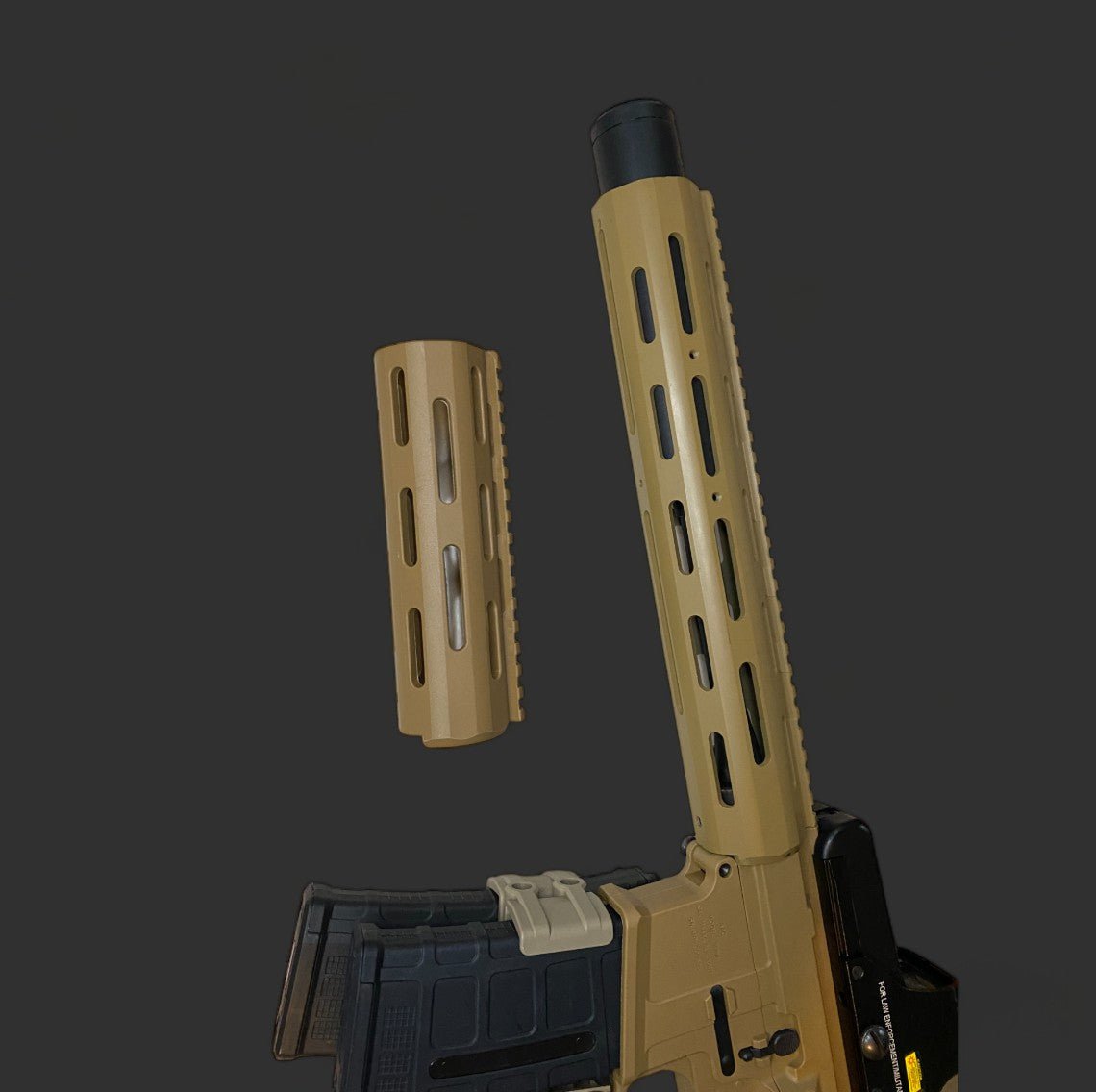 A partially disassembled tan and black rifle, featuring the Honey badger Handguard from BlasterMasters Upgrades, is displayed against a dark background. The handguard is detached and positioned above the remaining portion of the firearm.