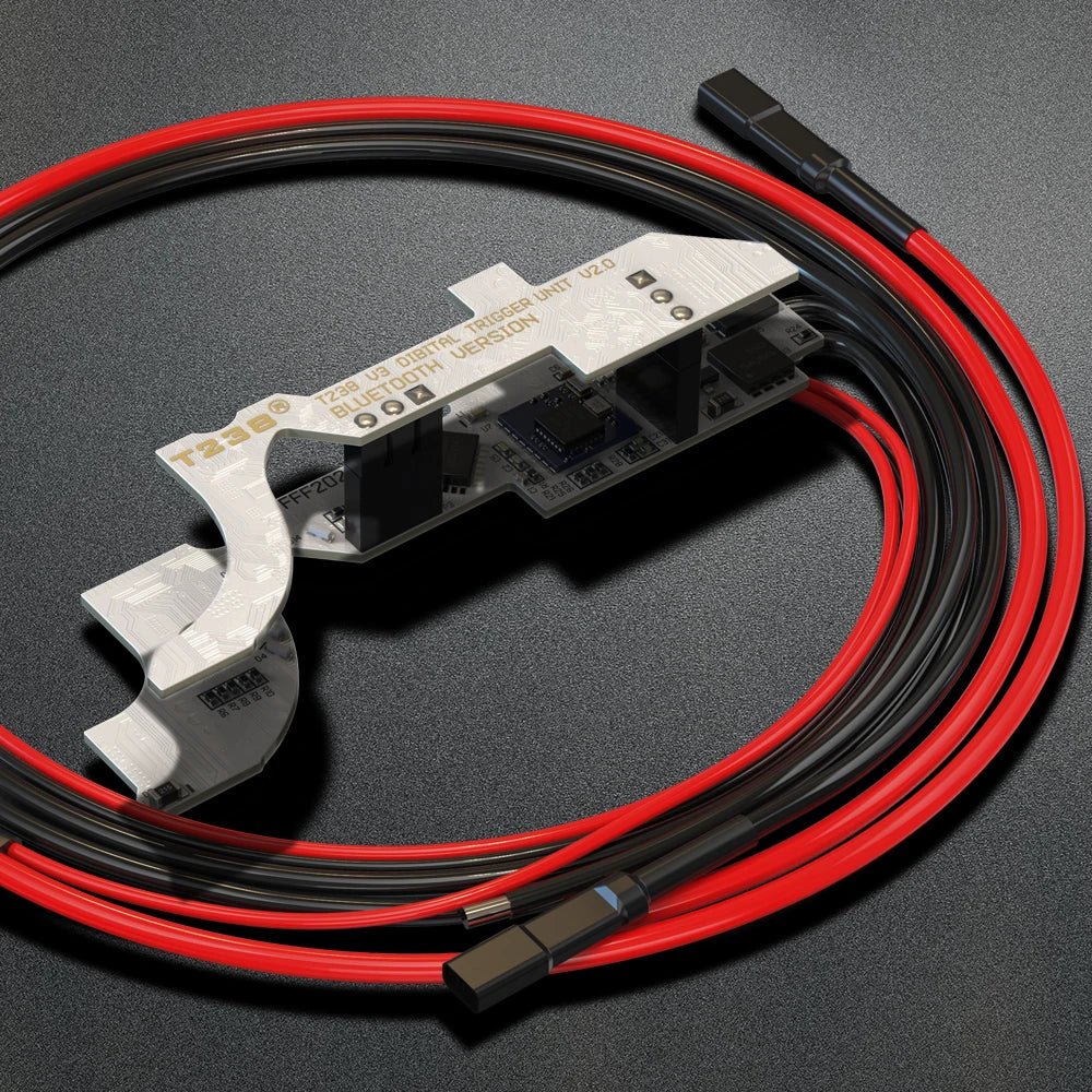 Close-up of an electronic circuit board with red and black wires attached, placed on a dark surface, possibly part of a BlasterMasters T238 V2.0 Bluetooth Mosfet Optical Sensor APP Control Programmable for Airsoft V3 Gearbox for precision control.